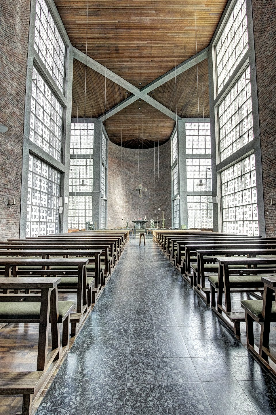 Moderne kerkinterieur met rijen kerkbanken gericht op een houten kruis.